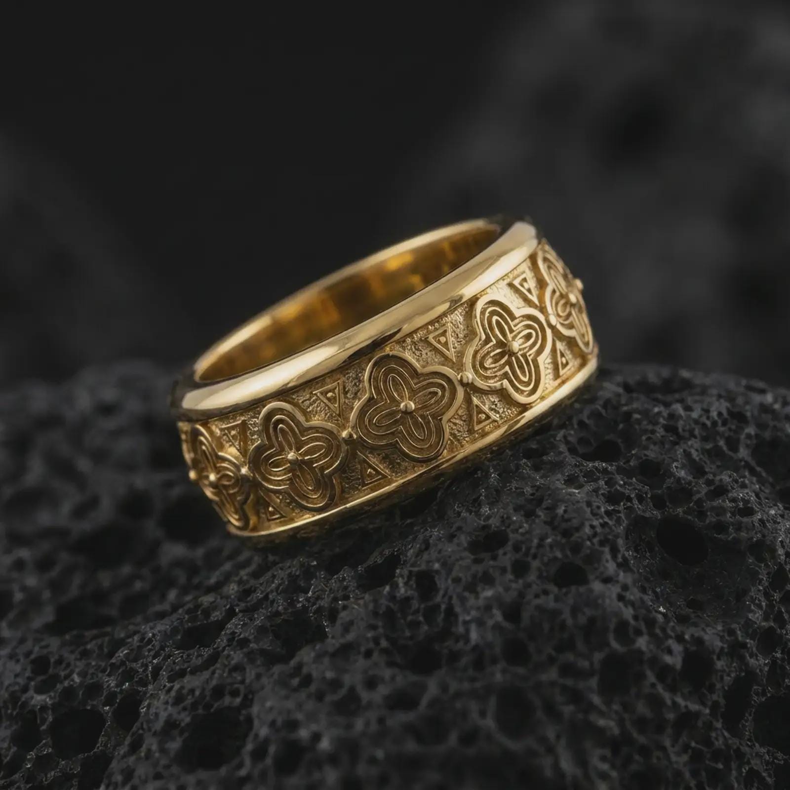 A gold plated floral spinner ring rests on rugged volcanic rock, featuring raised flower details, geometric accents, and an ornamental wide band design in a luxury macro studio close-up.