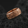 Load image into Gallery viewer, The rose gold plated floral wedding band is arranged on black volcanic rock, emphasizing its spinning ring construction, raised flower motifs, and refined unisex profile in a detailed macro image.
