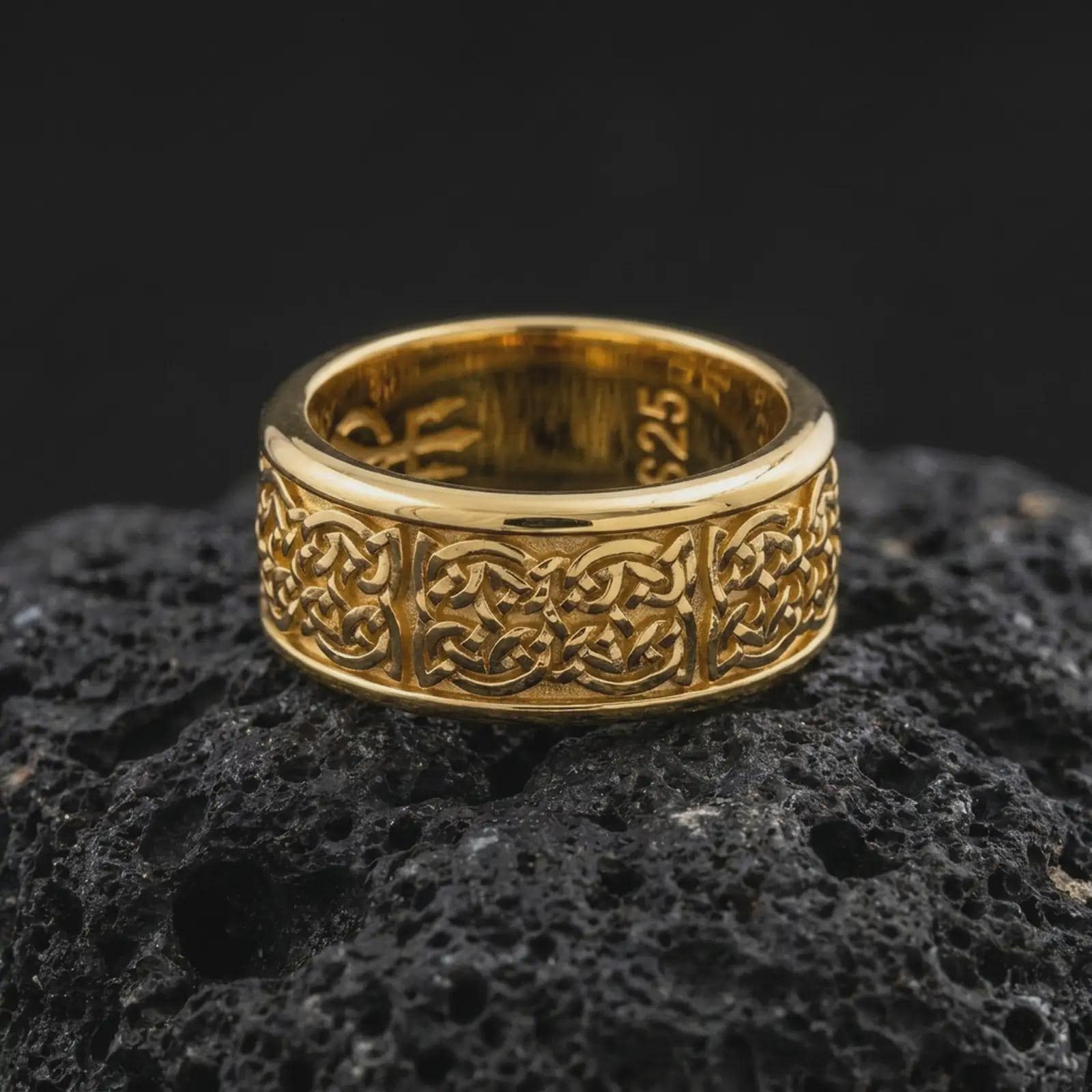 A gold plated Irish spinner ring sits on textured volcanic rock, showcasing the woven Celtic knot motif, symbolic band pattern, and elegant wide profile in a luxury macro shot.