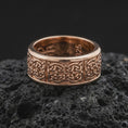 Load image into Gallery viewer, A rose gold plated Celtic wedding ring is placed on dark volcanic rock, featuring detailed interlaced knotwork, a smooth comfort-fit band, and a refined spinner ring design in close-up.
