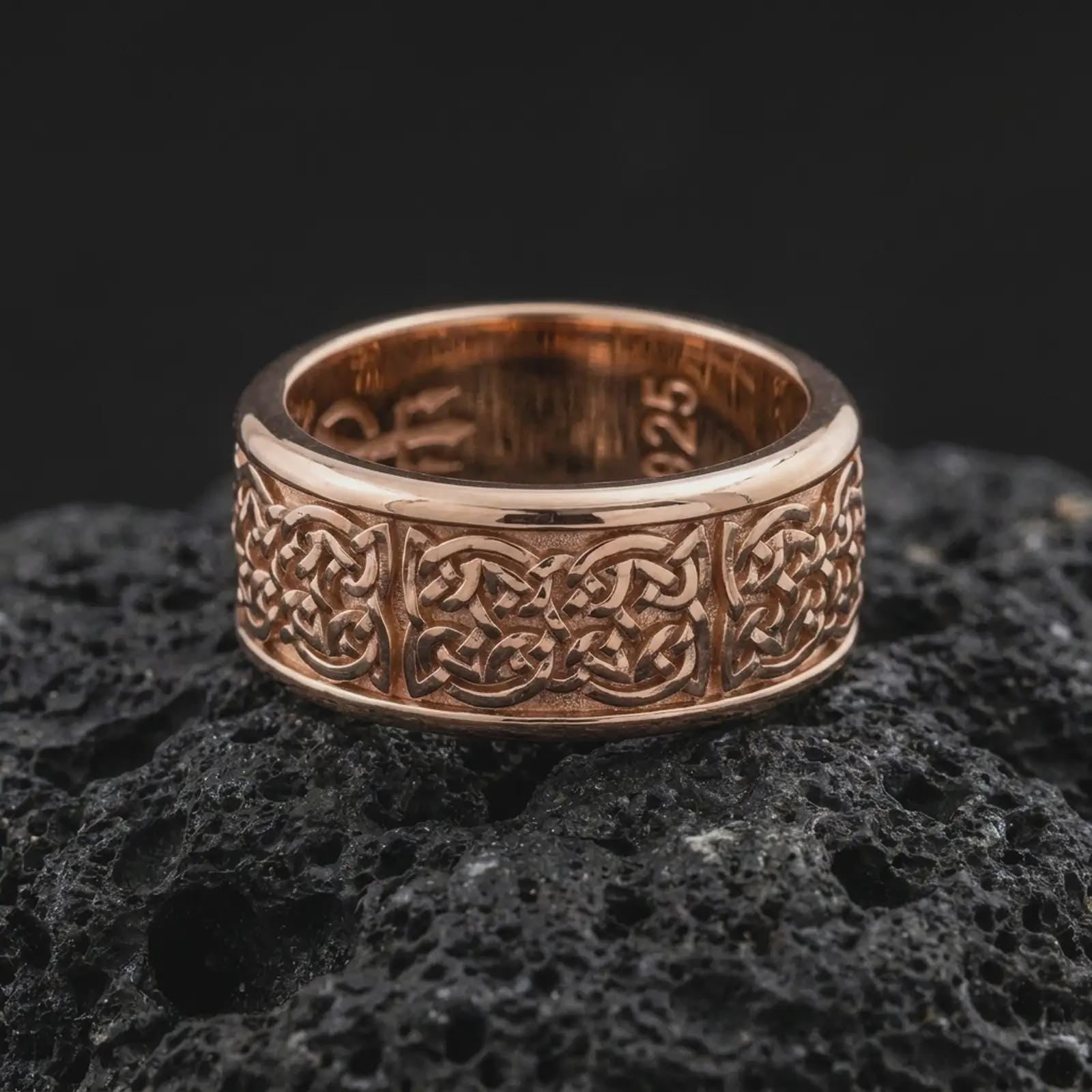 A rose gold plated Celtic wedding ring is placed on dark volcanic rock, featuring detailed interlaced knotwork, a smooth comfort-fit band, and a refined spinner ring design in close-up.