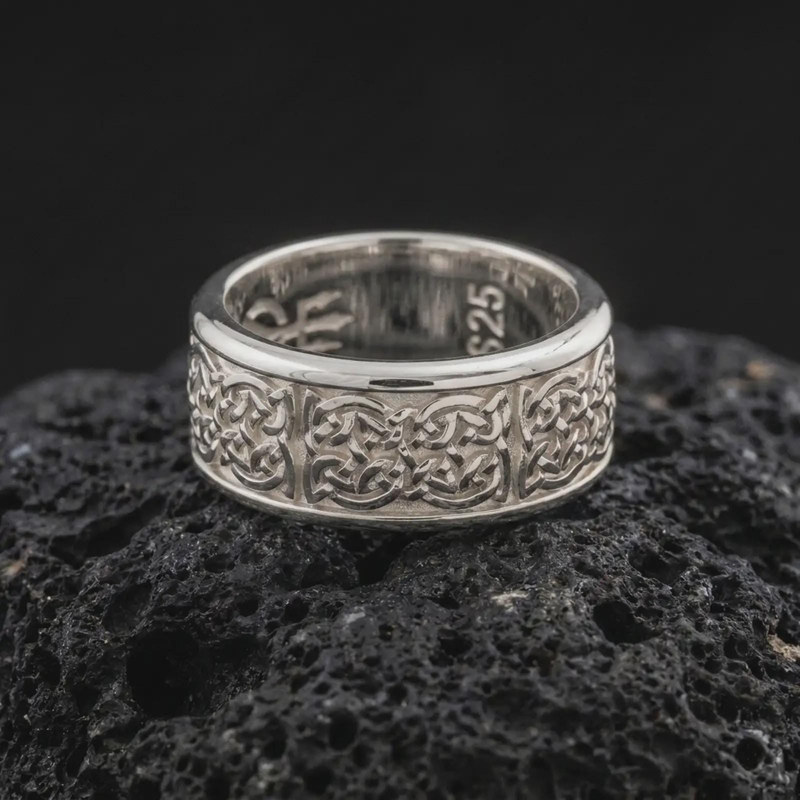 A polished silver Celtic knot wedding band is displayed on black volcanic rock, emphasizing the continuous knotwork, smooth rounded edges, and refined spinner band structure in a close-up image.