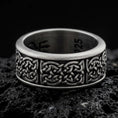 Load image into Gallery viewer, An oxidized sterling silver Celtic knot spinner ring rests on dark volcanic rock, highlighting the intricate interwoven Irish knot pattern and wide band design in a macro product photograph.
