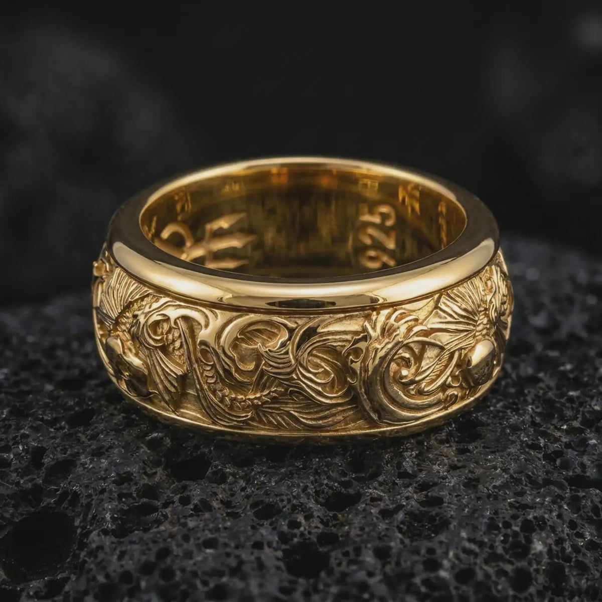 A gold plated koi fish spinner ring rests on rugged volcanic rock, featuring dimensional carp figures, curling ocean waves, and symbolic aquatic detailing in a luxury macro studio close-up.