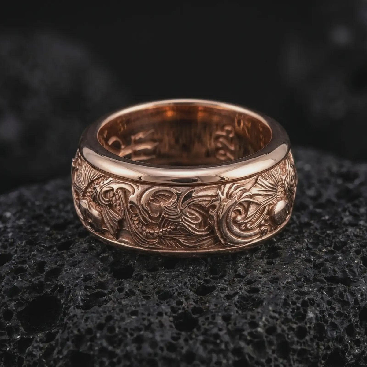 The rose gold plated carp wave ring is arranged on black volcanic rock, emphasizing the flowing water relief, raised fish elements, and refined unisex spinning band design in a detailed macro image.