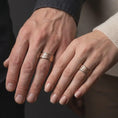 Load image into Gallery viewer, The rose gold plated floral spinner band is worn naturally on a finger, showcasing raised blossoms, scattered leaves, textured silverwork, and an elegant unisex wedding band profile.

