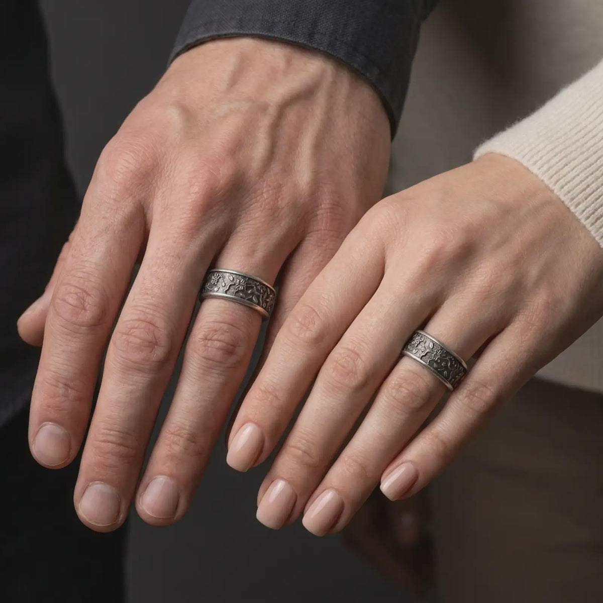 An oxidized floral spinner ring is worn on a finger, displaying the dark recessed botanical texture, raised silver blossoms, and calming wide band profile in a close-up lifestyle shot.