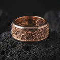Load image into Gallery viewer, The rose gold plated floral spinner ring is arranged on black volcanic rock, emphasizing its botanical pattern, smooth rounded borders, textured background, and refined unisex band design in a detailed macro image.

