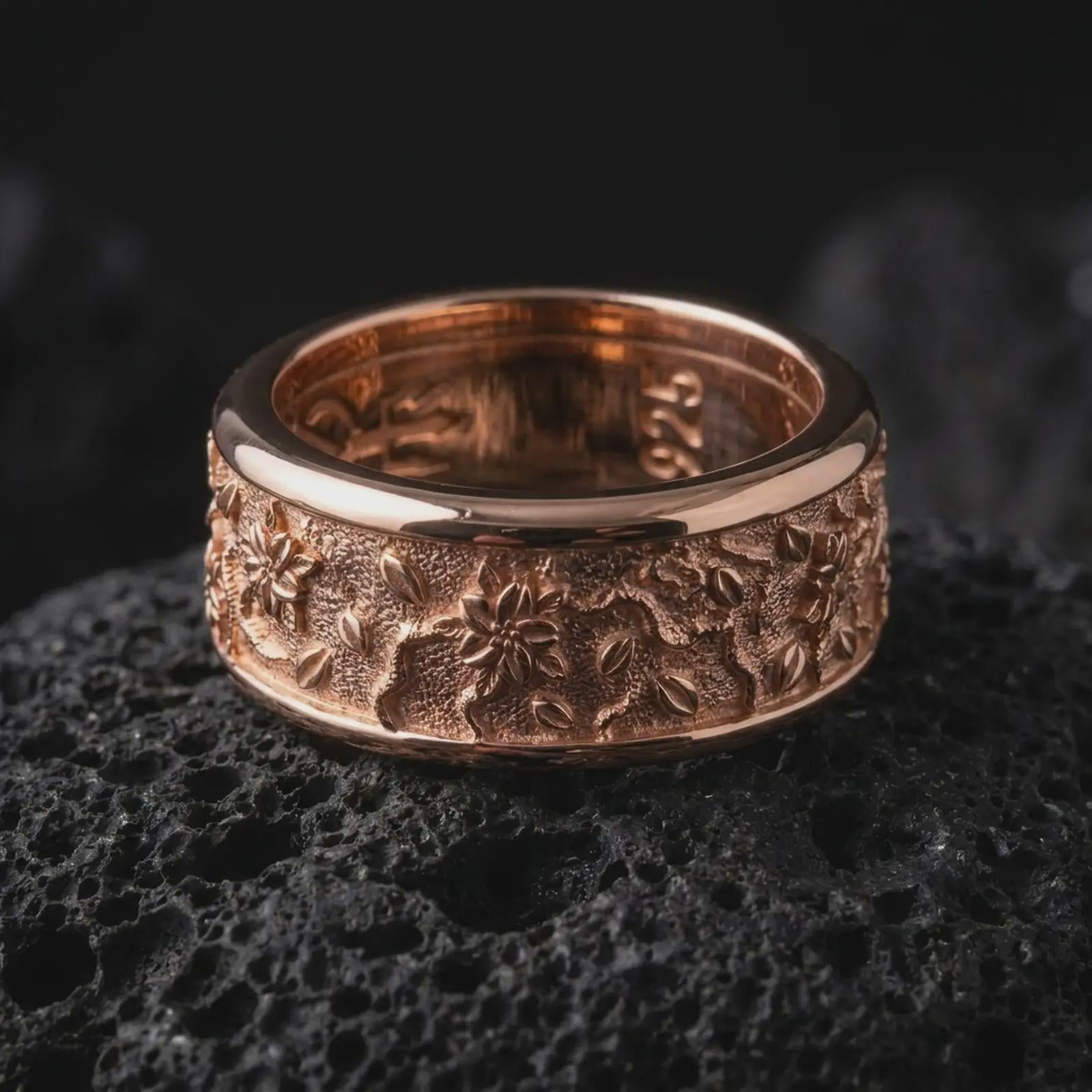The rose gold plated floral spinner ring is arranged on black volcanic rock, emphasizing its botanical pattern, smooth rounded borders, textured background, and refined unisex band design in a detailed macro image.