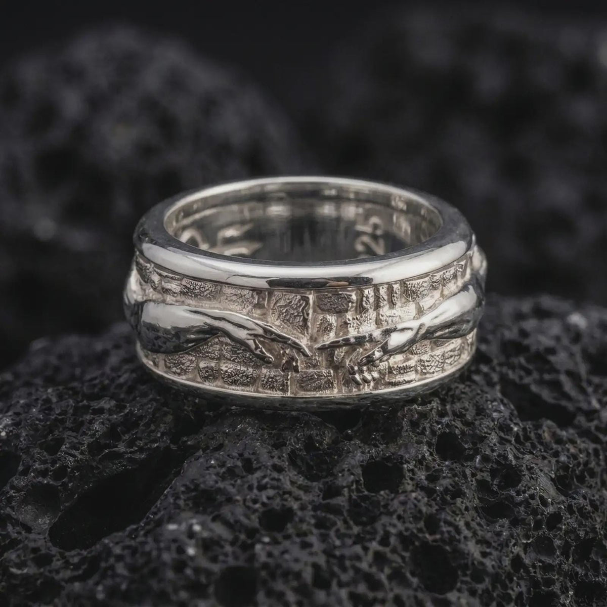 The polished silver Renaissance art ring is displayed on textured black volcanic rock, highlighting the raised hand motif, architectural background, and smooth spinning band profile in a premium macro photograph.