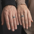 Load image into Gallery viewer, An oxidized Creation of Adam ring is worn on a finger, displaying the dark recessed texture, raised reaching hands, and meaningful wide spinner band in a close-up lifestyle shot.
