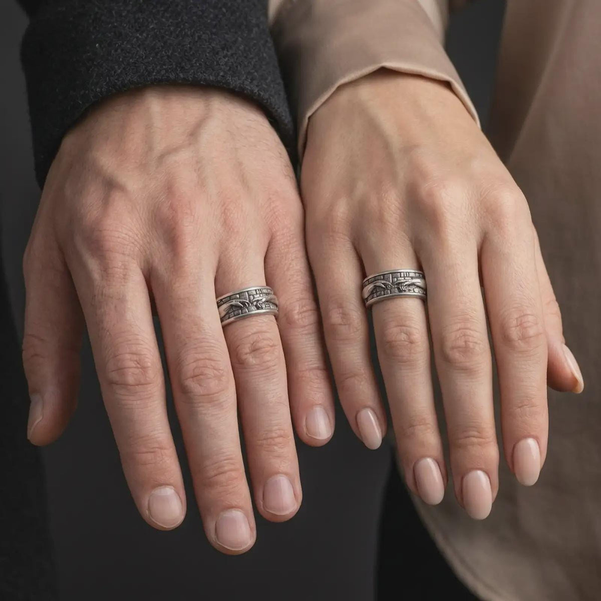 An oxidized Creation of Adam ring is worn on a finger, displaying the dark recessed texture, raised reaching hands, and meaningful wide spinner band in a close-up lifestyle shot.