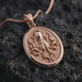 Load image into Gallery viewer, The rose gold plated octopus medallion is arranged on black volcanic rock, emphasizing the sculpted tentacles, suction cup details, round frame, and nautical sea life design in a refined macro image.
