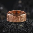 Load image into Gallery viewer, The rose gold plated Aztec pattern ring is arranged on black volcanic rock, emphasizing its tribal-inspired engravings, textured recessed background, and refined unisex spinner band design in a detailed macro image.
