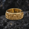 Load image into Gallery viewer, A gold plated Asian dragon spinner ring rests on rugged volcanic rock, featuring ornate dragon motifs, symbolic craftsmanship, and an engravable wide band in a luxury macro studio close-up.
