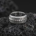 Load image into Gallery viewer, A polished silver lizard scale rotating ring is displayed on black volcanic rock, emphasizing the layered reptile-inspired surface, smooth band edges, and distinctive spinner construction in a refined macro photograph.
