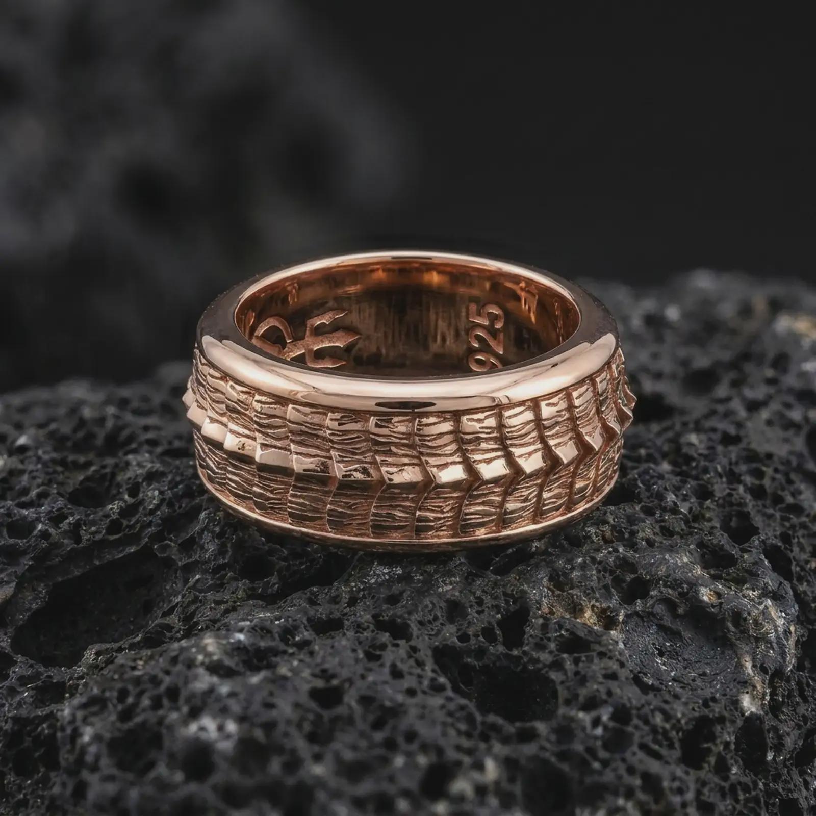 A rose gold plated reptile spinner ring is arranged on dark volcanic rock, featuring a detailed lizard scale pattern, elegant rotating band structure, and warm metallic finish in a close-up product photograph.