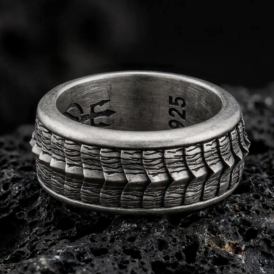 An oxidized sterling silver lizard scale spinner ring rests on dark volcanic rock, highlighting the rotating reptile texture, rugged pattern, and bold band design in a dramatic macro close-up.