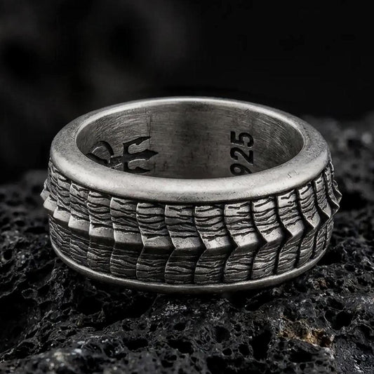 An oxidized sterling silver lizard scale spinner ring rests on dark volcanic rock, highlighting the rotating reptile texture, rugged pattern, and bold band design in a dramatic macro close-up.