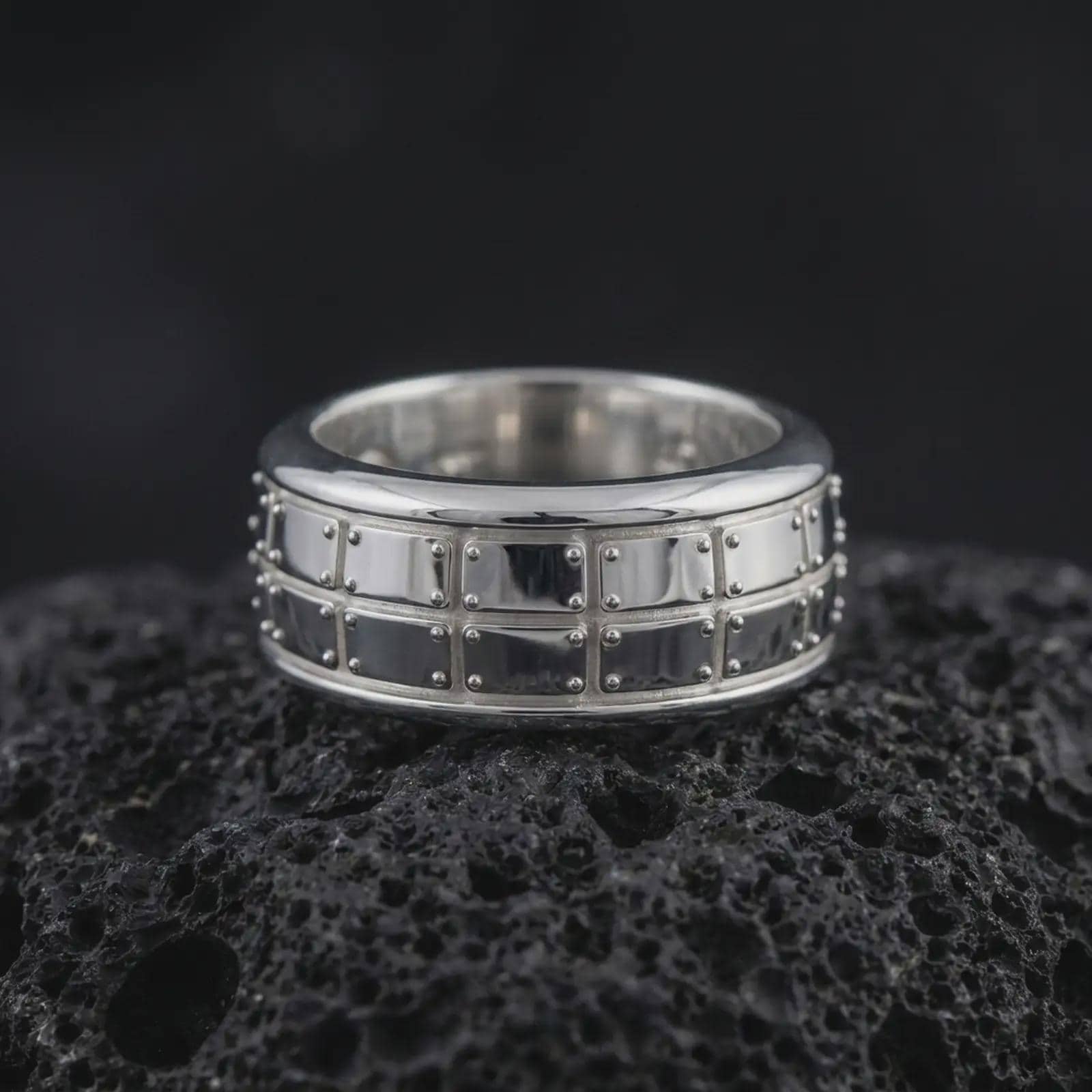 A polished silver plate pattern spinner ring is displayed on black volcanic rock, emphasizing the clean geometric sections, smooth band edges, and refined rotating construction in a detailed product photograph.