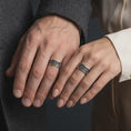 Load image into Gallery viewer, An oxidized scroll spinner ring is worn on a finger, displaying the dark recessed background, raised silver vine details, and calming wide band profile in a close-up lifestyle shot.
