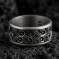 Load image into Gallery viewer, An oxidized sterling silver scroll spinner ring rests on dark volcanic rock, showing raised vine-like curves, ornamental scrollwork, and a dark recessed wide band in a macro studio close-up.
