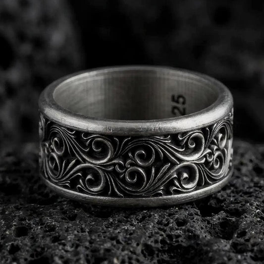 An oxidized sterling silver scroll spinner ring rests on dark volcanic rock, showing raised vine-like curves, ornamental scrollwork, and a dark recessed wide band in a macro studio close-up.