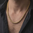 Load image into Gallery viewer, A gold plated 6mm Byzantine chain necklace is worn on a man’s neck with dark clothing, highlighting the woven link construction and strong statement profile in a refined close-up.
