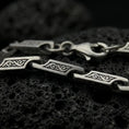 Load image into Gallery viewer, An oxidized ornate scroll chain necklace rests on dark volcanic rock, showing rectangular engraved bar links, recessed swirl details, and articulated connectors in a macro studio close-up.
