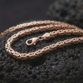 Load image into Gallery viewer, The rose gold plated 5mm square Byzantine necklace is arranged on black volcanic rock, emphasizing the structured link construction, flexible chain movement, and refined statement design in a detailed macro image.
