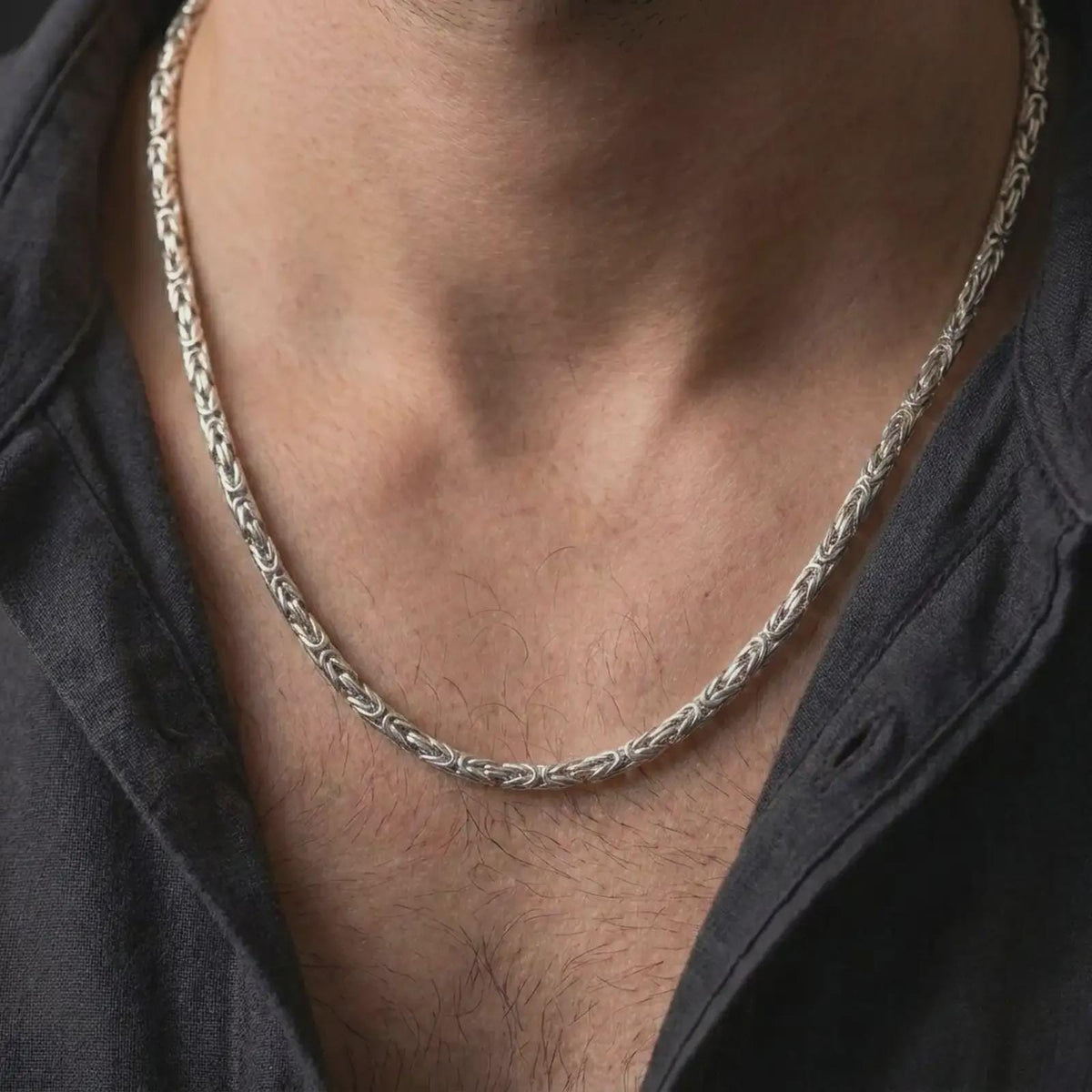 The polished silver Byzantine necklace is worn on a man’s chest, showing the compact 4mm width, rounded interlocking links, and refined everyday jewelry style in a premium lifestyle photograph.