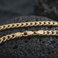 Load image into Gallery viewer, A gold plated 5mm Cuban chain necklace lies on rugged volcanic rock, featuring smooth flattened links and a refined masculine chain profile in a luxury macro studio close-up.

