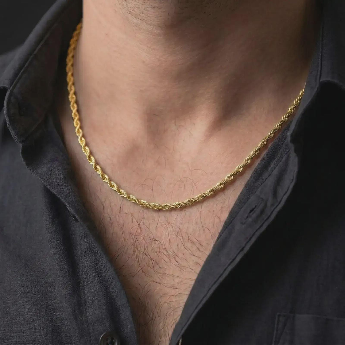 A gold plated 3mm rope chain necklace is worn on a man’s neck with dark clothing, highlighting the classic spiral pattern and polished minimalist profile in a refined close-up.