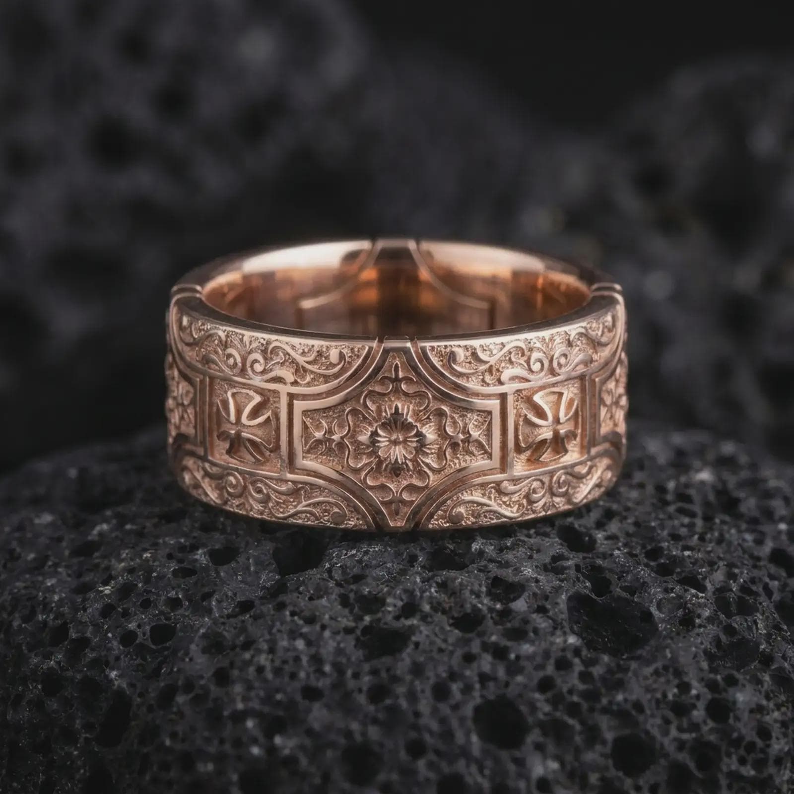 The rose gold plated ornate cross band ring is arranged on black volcanic rock, emphasizing its symmetrical ornamental relief, floral centerpiece, decorative cross motifs, and wide medieval-inspired band design.