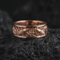 Load image into Gallery viewer, The rose gold plated botanical wedding band is arranged on black volcanic rock, emphasizing its detailed floral relief, flowing leaves, organic ornamentation, and elegant nature-inspired design.

