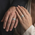 Load image into Gallery viewer, The polished silver floral wedding band is worn naturally on a finger, showing the continuous botanical relief, detailed flowers and foliage, smooth edges, and wide sterling silver band profile in a premium lifestyle photograph.
