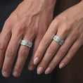 Load image into Gallery viewer, The polished silver ornate spinner ring is worn naturally on a finger, showing the repeating fleur-de-lis motifs, detailed scrollwork, smooth edges, and refined unisex wedding band style in a premium lifestyle shot.
