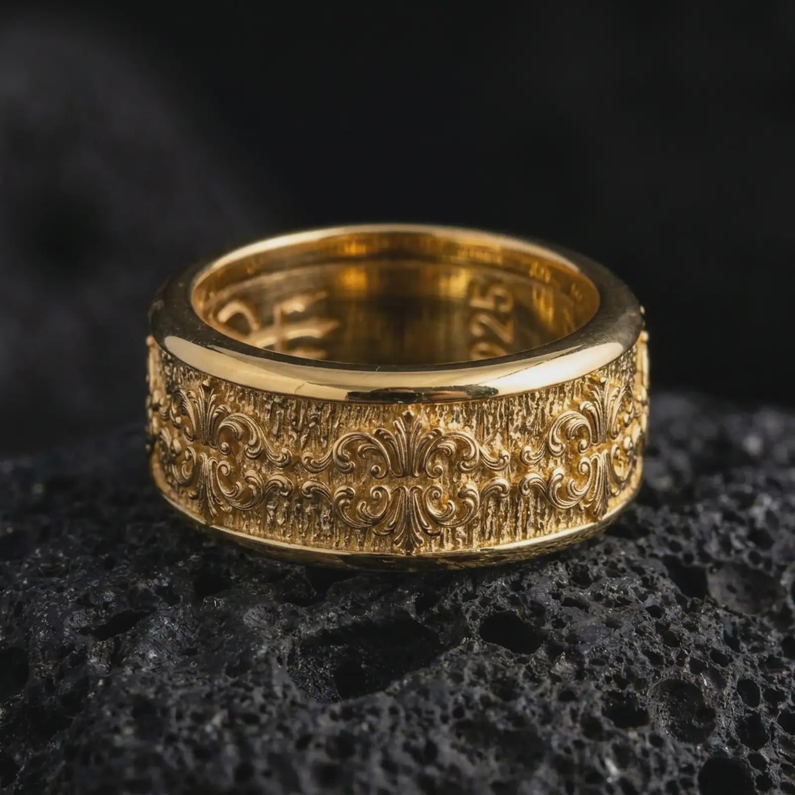 A gold plated Baroque spinner ring rests on rugged volcanic rock, featuring repeating fleur-de-lis motifs, elaborate scrollwork, and a wide textured wedding band profile in a luxury macro studio close-up.