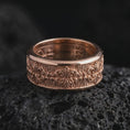 Load image into Gallery viewer, The rose gold plated fleur-de-lis wedding band is arranged on black volcanic rock, emphasizing the raised ornamental pattern, vintage-inspired texture, and refined unisex spinner ring construction in a detailed macro image.
