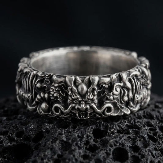 An oxidized sterling silver Asian dragon ring rests on dark volcanic rock, featuring a sculpted dragon face, curling whiskers, ornate scales, and deep recessed details in a dramatic macro studio close-up.