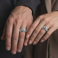 Load image into Gallery viewer, The polished silver skull and serpent ring is worn naturally on a finger, showing the dimensional skull motifs, detailed snake scales, floral accents, and substantial unisex band profile in a premium lifestyle photograph.
