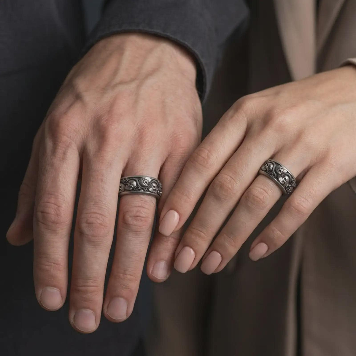 An oxidized sterling silver skull snake rose ring is worn on a finger, displaying the dark recessed background, raised skulls, textured serpent, and sculpted roses in a close-up gothic lifestyle photograph.