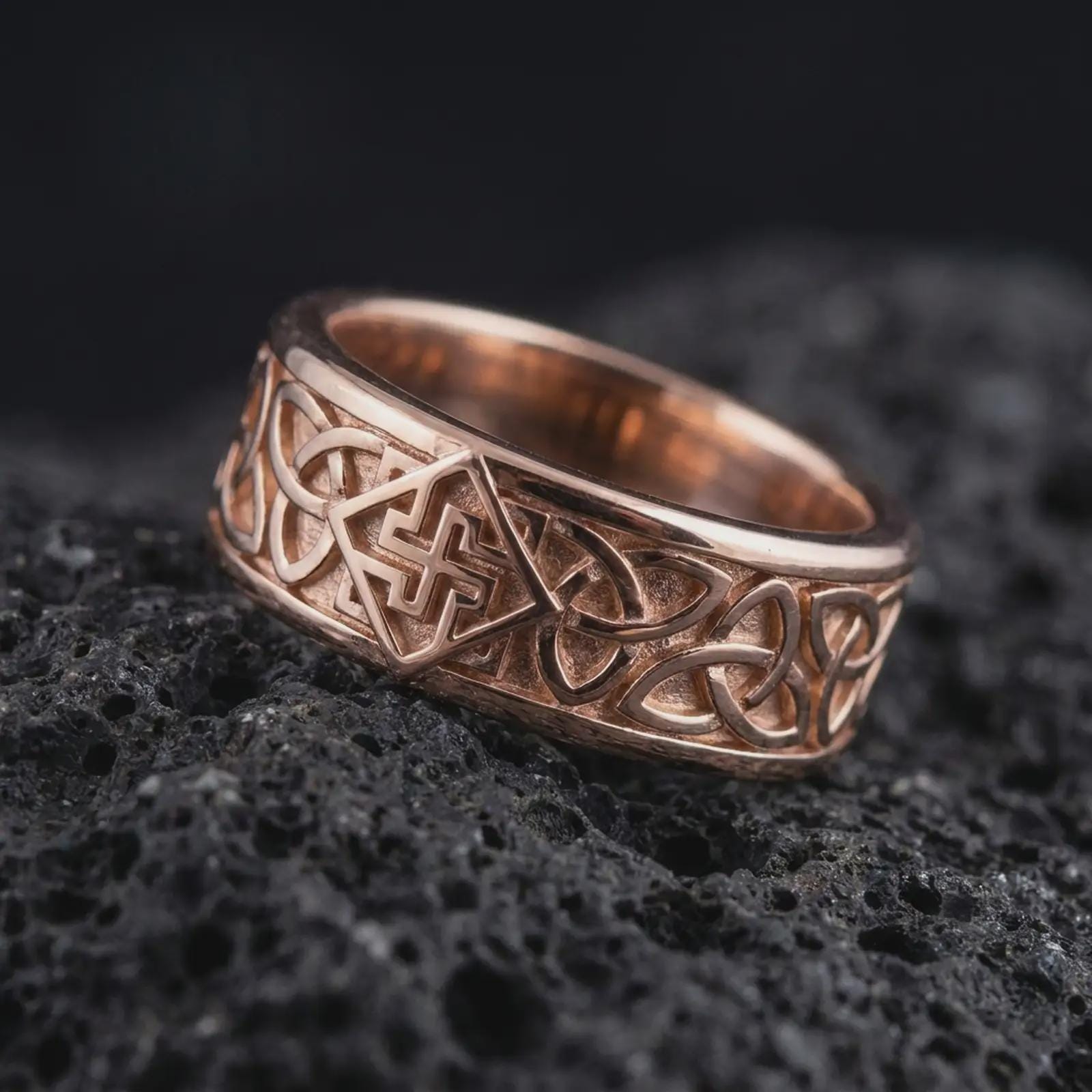 The rose gold plated Celtic knot ring is arranged on black volcanic rock, emphasizing the engraved interlace design, dimensional band texture, and historical-inspired craftsmanship in a refined macro image.