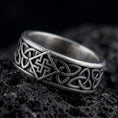 Load image into Gallery viewer, An oxidized sterling silver Celtic knot ring rests on dark volcanic rock, showing raised interlaced knotwork and a dark recessed band background in a macro studio close-up.
