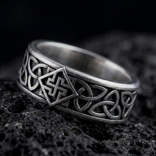 An oxidized sterling silver Celtic knot ring rests on dark volcanic rock, showing raised interlaced knotwork and a dark recessed band background in a macro studio close-up.