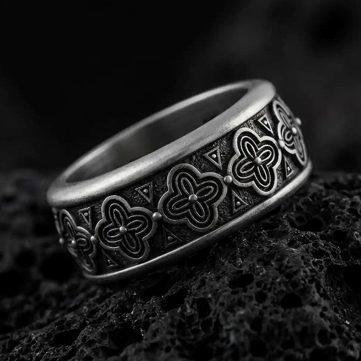 An oxidized sterling silver floral spinner ring rests on dark volcanic rock, showing raised flower motifs, triangle accents, and a dark recessed band background in a macro studio close-up.