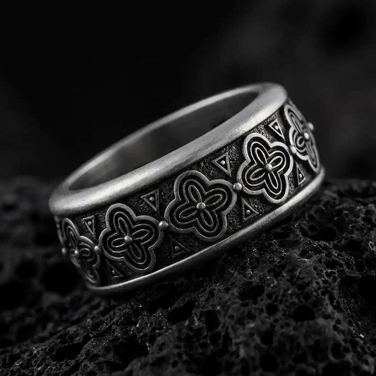 An oxidized sterling silver floral spinner ring rests on dark volcanic rock, showing raised flower motifs, triangle accents, and a dark recessed band background in a macro studio close-up.