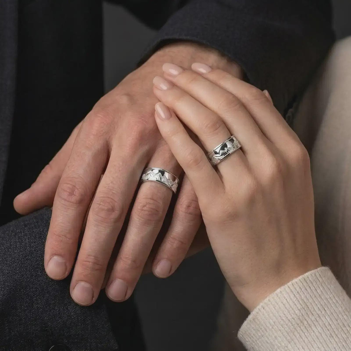 The polished silver mountain spinner ring is worn on a finger, highlighting the scenic Grand Teton engraving and refined unisex wedding band look in a lifestyle photograph.