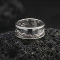 Load image into Gallery viewer, The polished silver Grand Teton mountain ring is displayed on black volcanic rock, highlighting the scenic mountain engraving and spinning fidget band design in a clean macro studio image.
