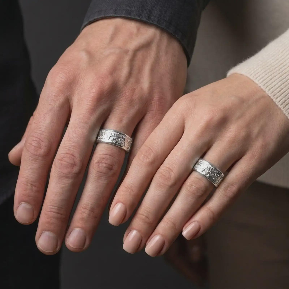 The polished silver flower wedding band is worn on a finger, showing the repeating floral details, smooth edges, and refined unisex spinner ring design in a premium lifestyle photograph.